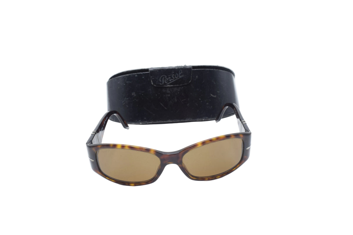 Tortoiseshell sunglasses with brown tinted lenses and a black rectangular case behind them, photographed on a white background.