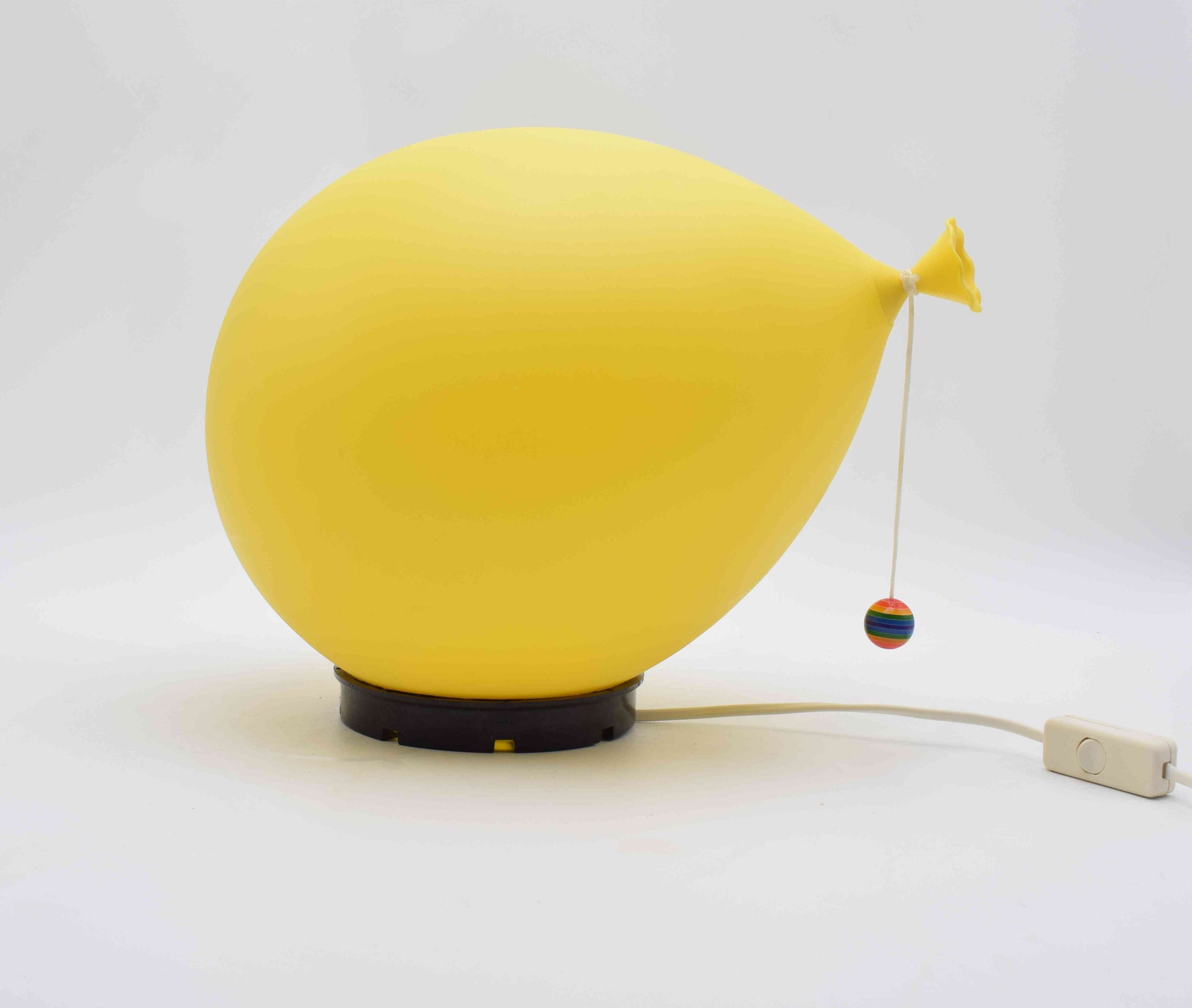 Yellow balloon-shaped lamp with a string and colorful bobbin on a white background