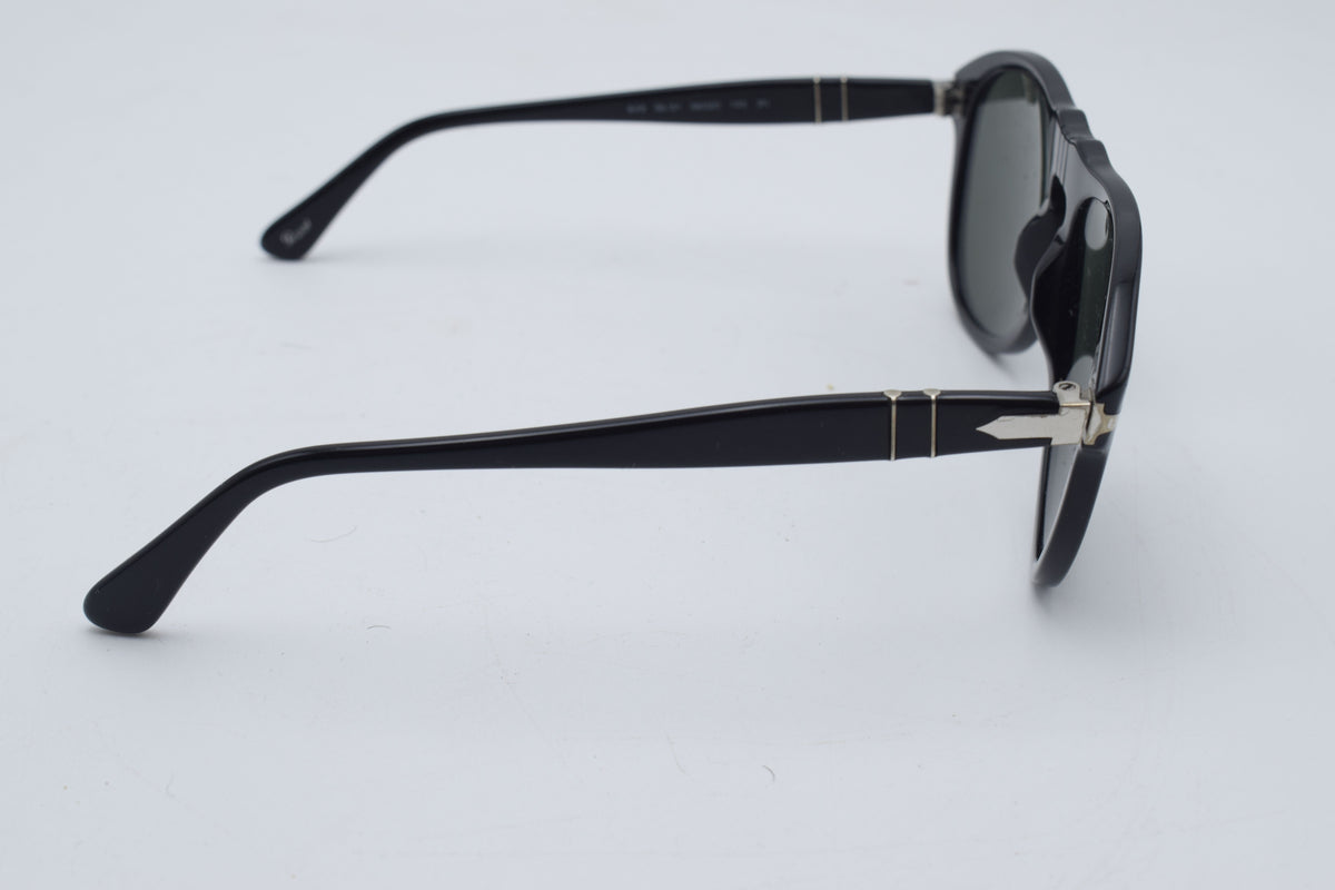 Black acetate sunglasses with dark lenses and small gold metal accents on the temples, shown from a side profile on a light gray background.